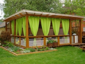 Красивая деревянная беседка с зелеными шторами