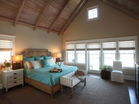 Просторная светлая спальня со скошенным потолком и бирюзовым постельным на кровате