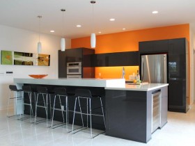 Современная светлая кухня с черной мебелью и оранжевой стеной