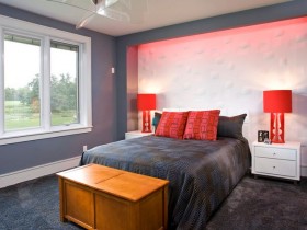 Яркая спальня в серых тонах с красными светильниками и деревянным сундуком