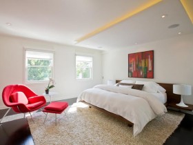 Современная спальня со скрытой потолочной подсветкой и красным стульчиком